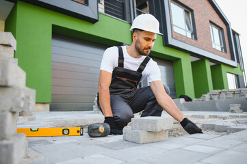 The master in gloves lays paving stones in layers. Garden brick pathway paving by professional...