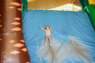 Child joyfully sliding down an inflatable slide in a playful indoor playground during daytime fun activities