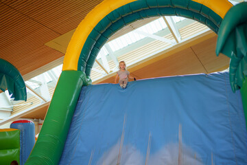Child happily prepares to slide down a large inflatable structure at an indoor play center during a sunny afternoon