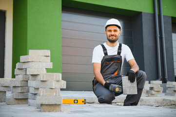 Worker skillfully laying paving stones using a hammer and wearing gloves, showcasing precision