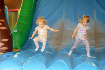 Two young girls joyfully jumping on a colorful inflatable slide at a play center during a sunny afternoon
