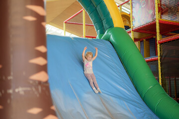 Child joyfully sliding down a colorful inflatable slide in an indoor play area during afternoon playtime