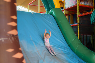 Child enjoys a fun slide at an indoor playground during a sunny afternoon in the play area