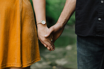 Close-up of couple holding hands showing engagement ring, wristwatch, mustard skirt, denim jeans...
