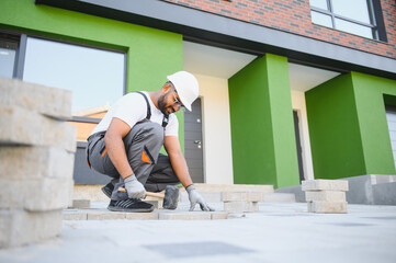 Indian Worker skillfully laying paving stones using a hammer and wearing gloves, showcasing precision