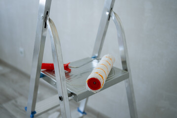 Paint roller and tray resting on a metal ladder, poised for action in a room undergoing renovation,...