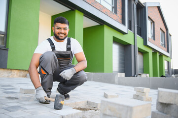 Indian master in gloves lays paving stones in layers. Garden brick pathway paving by professional paver worker. Laying gray concrete paving slabs in house courtyard on sand foundation base