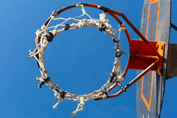 Basketball hoop with damaged net under blue sky