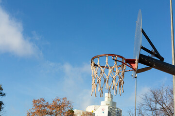 Basketball hoop with damaged net under blue sky