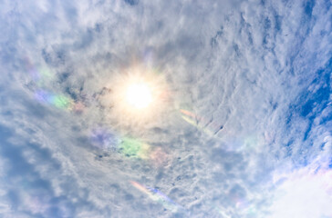 Partly cloudy sky with shining sun and atmospheric color flares in the clouds.
Sky is blue and...
