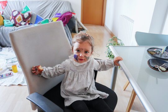 Little girl with painted face sitting on a chair at home
