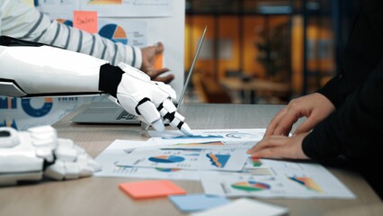 A human hand collaborates with a robotic arm as they analyze data in a modern workspace,...