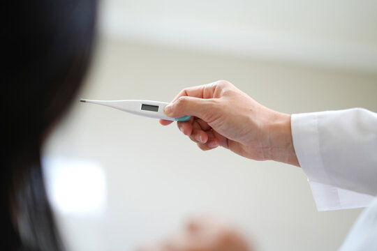 Professional asian young woman doctor is holding a oral digital thermometer, taking a sick patient's temperature at the hospital or clinic, ensuring accurate and hygienic temperature readings.