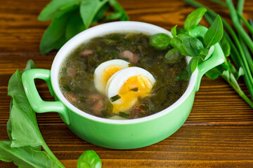 Top view of a plate of green borscht with egg and sorrel on a dark wooden table