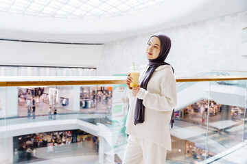 Muslim girl with smoothie near glass railing in mall