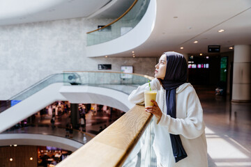 Side view of Woman in hijab drinking smoothie in indoor shopping center