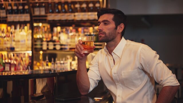 Smart man in white shirt drinking cocktail Old fashioned waiting friends or couple while chatting on smartphone in special party beverage vibrant at nightclub on Friday meeting night time. Vinosity.