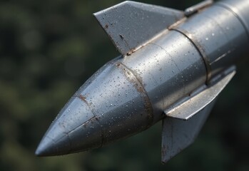 Close-up view of a silver missile on display highlighting intricate details and weathered texture surrounded by greenery