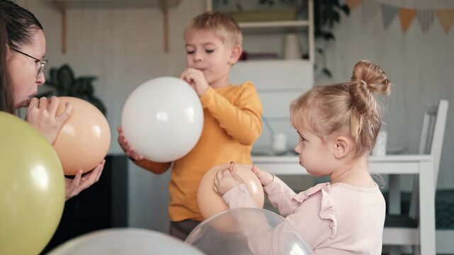 Family Fun Children Joyfully Blowing Up Balloons. Kids inflating balloons, prepare for birthday party. 3,6, 14 years old siblings racing blowing balloon, decorate the room. Bonding time together. Joy