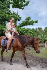 A mother and her little girl enjoy a delightful ride on a gentle horse at a vibrant farm. Sunlight...