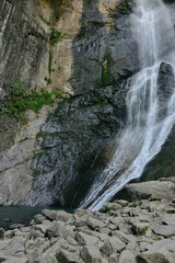 Waterfall cascading over rocky cliff with scattered stones and natural green moss, showcasing serene and untouched nature landscape in daylight.
