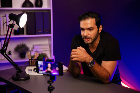 Broadcaster talking to listener on live streaming online, recording by smartphone setting on social media in host channel by creative positive thinking concept at purple neon light studio. Surmise. - Powered by Adobe