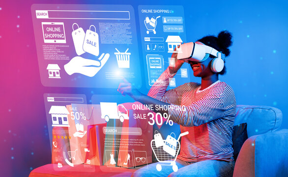 Happy girl using VR glasses to connect online shopping screen. Woman wearing augmented reality headset while selecting and buying product in hologram and sitting at sofa with shopping bag. Ingenuity.