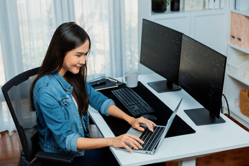 Smiling young Asian in IT developer creating with typing online information on laptop with coding...