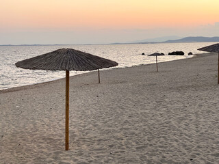 A serene beach scene during sunset with an empty parasol and soft waves. Ideal for themes of peace,...