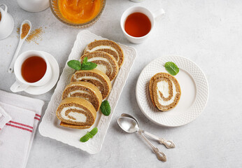 Top view of a slice of Baked pumpkin roll on a white plate with cups of tea, breakfast kitchen scene