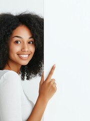 Smiling woman with curly hair pointing to a blank wall in a bright indoor space during daylight
