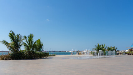 West beach on Palm Jumeirah Island, Dubai on sunny summer day. Fountain on wooden boardwalk. Walking around city