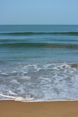 Ocean Waves with White Foam on Sandy Beach under Blue Sky