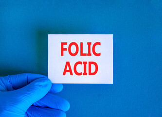 Folic acid symbol. Concept words Folic acid on beautiful white card. Doctor's hand in blue medical glove. Beautiful blue background. Medical healthy lifestyle folic acid concept.