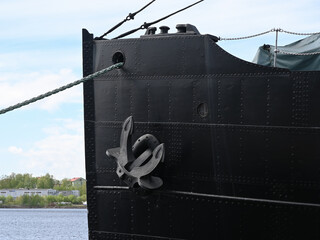 the imposing bow of a large black ship moored at a harbor, featuring a prominent steel anchor attached to its riveted metal hul