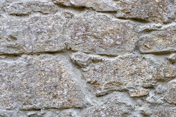 Close-up of a section of masonry with gray, uneven stones held together with cement mortar to form a textured background