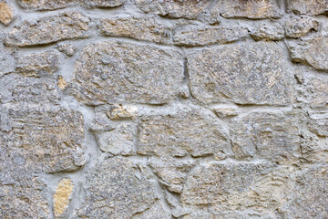 Close-up of a section of masonry with gray, uneven stones held together with cement mortar to form a textured background