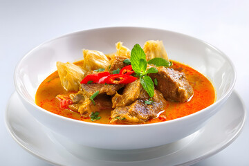 Bowl of spicy curry with beef, vegetables, and chili pepper garnish, served in bowl.