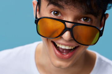 Young man wearing large orange sunglasses smiling joyfully against blue background, expressing...