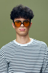 Young man wearing large orange sunglasses and striped shirt with curly hair looking indifferent on...