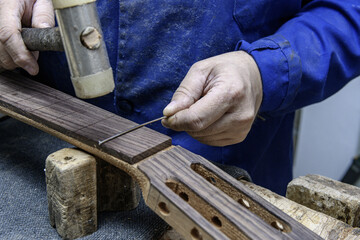 Luthier hammering frets into wooden guitar neck