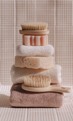cepillos exfoliantes de baño con mango de madera natural ecológica, toallas claras y esponjas naturales sobre fondo de baño o spa con pared y suelo de azules de gresite en tonos pastel beige