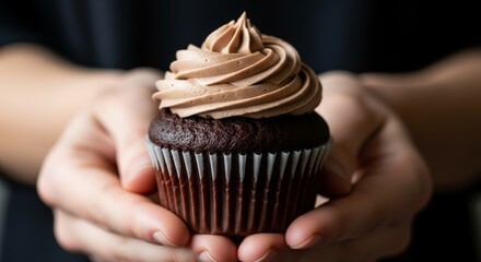Close-up of a delicious chocolate cupcake with swirled frosting, gently held in hands. Perfect for bakery, dessert, and celebration themes.
