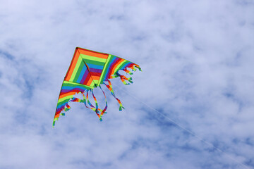 Bright kite against the cloudy sky. Toy for children and adults. Outdoor activities. Colorful kite flies in the sky, windy weather. Cloudless mood. Fly. Bright multi-colored kite flies in the air