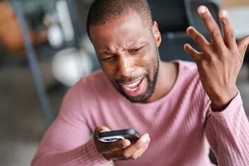 Frustrated Black Man in Stylish Office Holding Smartphone Expressing Strong Emotions