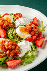 Fresh salad with boiled eggs, tomatoes, and strawberries served with creamy dressing on a white plate. Vibrant, healthy dish ideal for lunch or dinner menus.