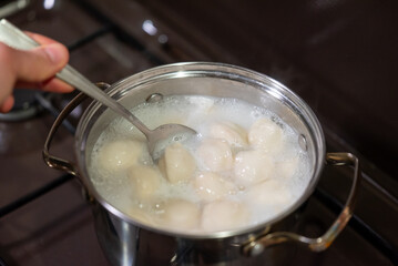 Stirring dumplings in bubbling pot of water. A close-up of a spoon actively stirring white, round...
