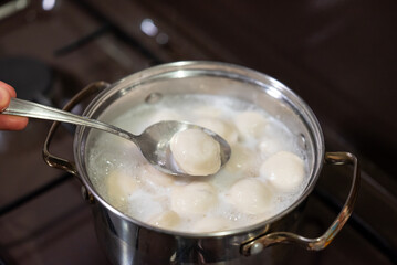 Spoon stirring pelmeni in boiling water. A close-up shot of a spoon checking readiness of pelmeni...