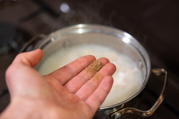 Hand adding spices to cooking pelmeni. A close-up shot of a hand sprinkling pepper, salt and other...