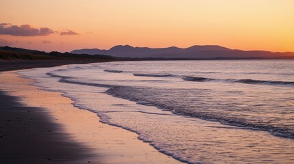 Obraz premium Stunning beach at sunset with calming waves and mountains in the background. Perfect for relaxation and nature lovers.